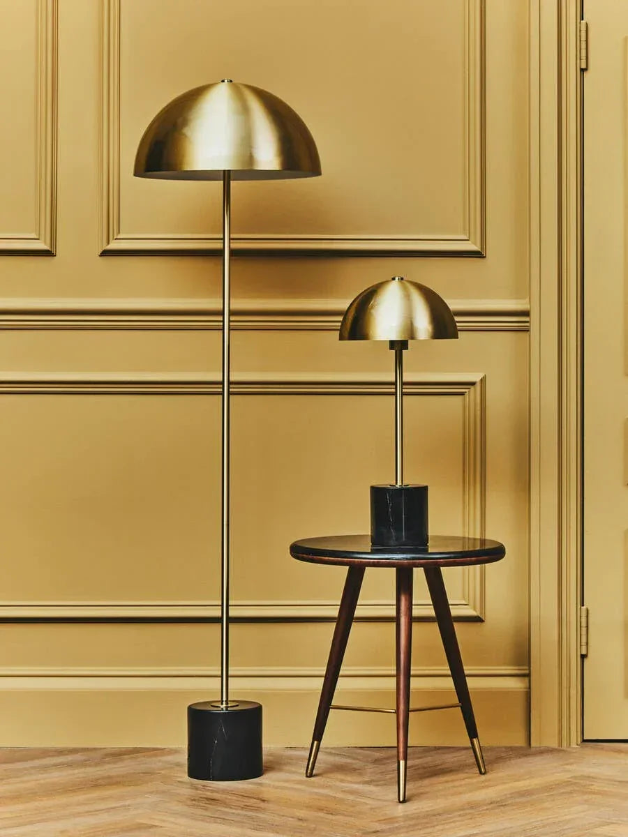 Brass floor lamp and table lamp with black marble bases beside round wooden side table