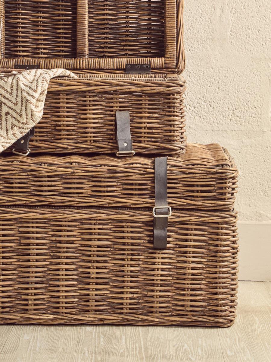 Stacked wicker storage baskets with leather straps on wooden floor