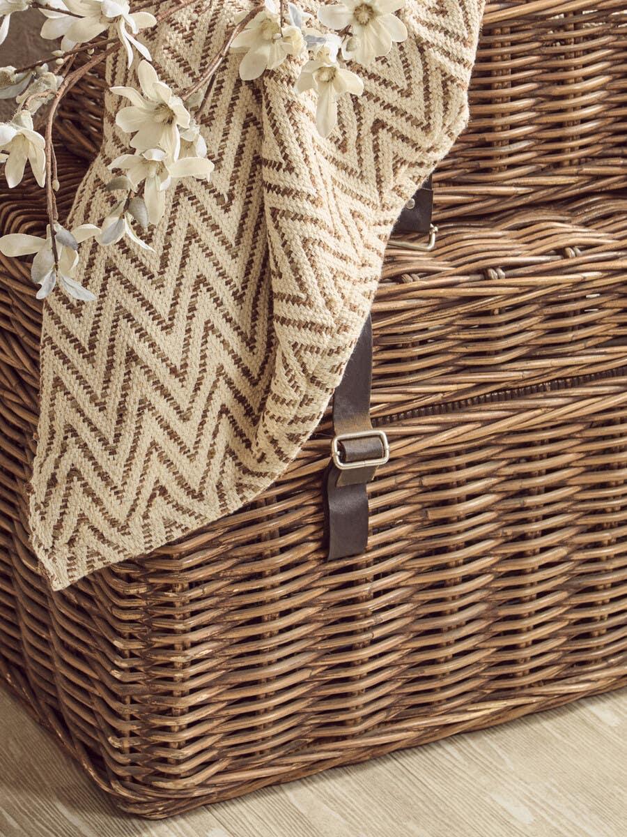 Wicker storage basket with leather straps, chevron pattern throw and artificial flowers