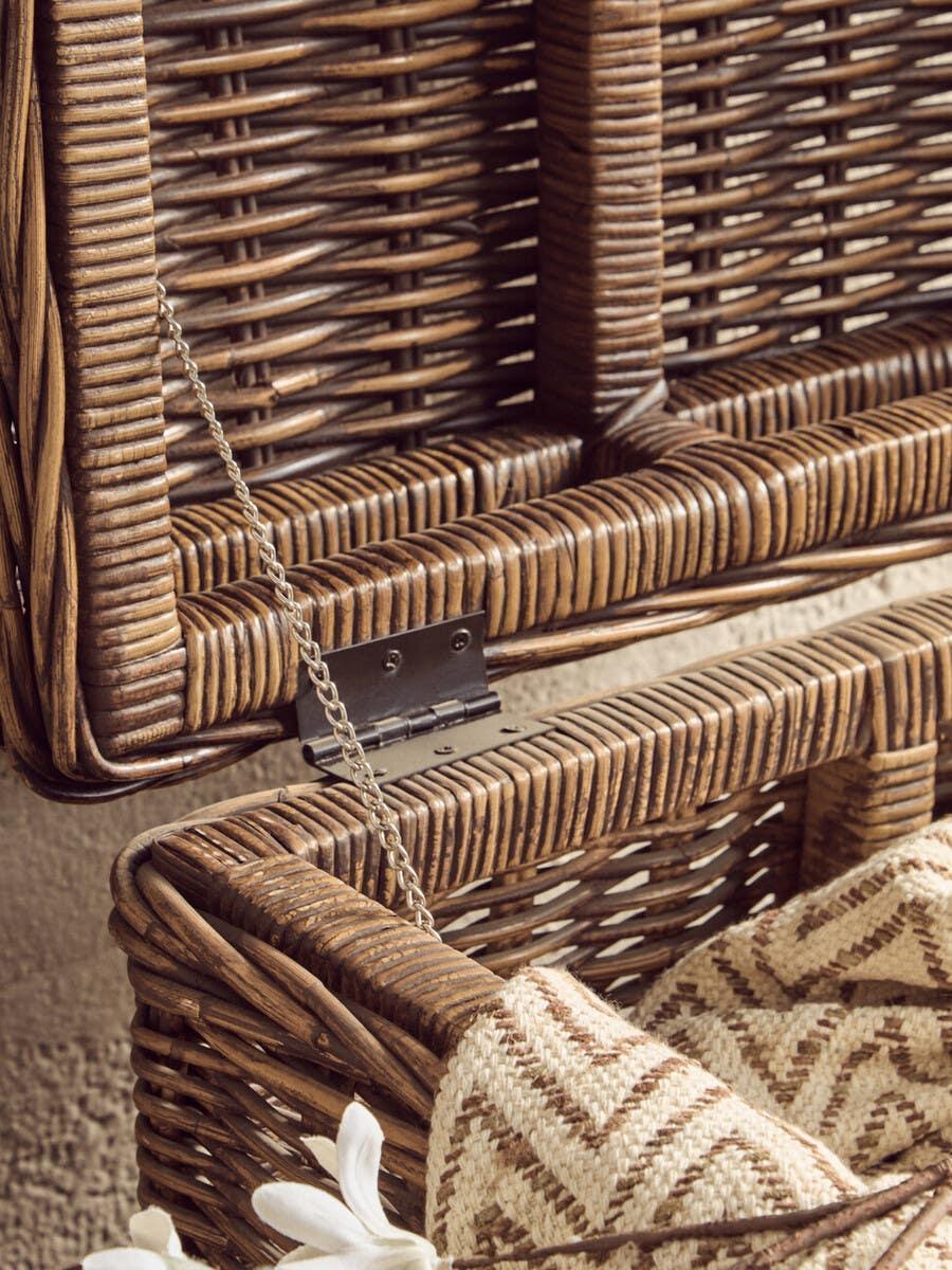 Closeup of open wicker storage basket with metal hinge and patterned throw blanket inside