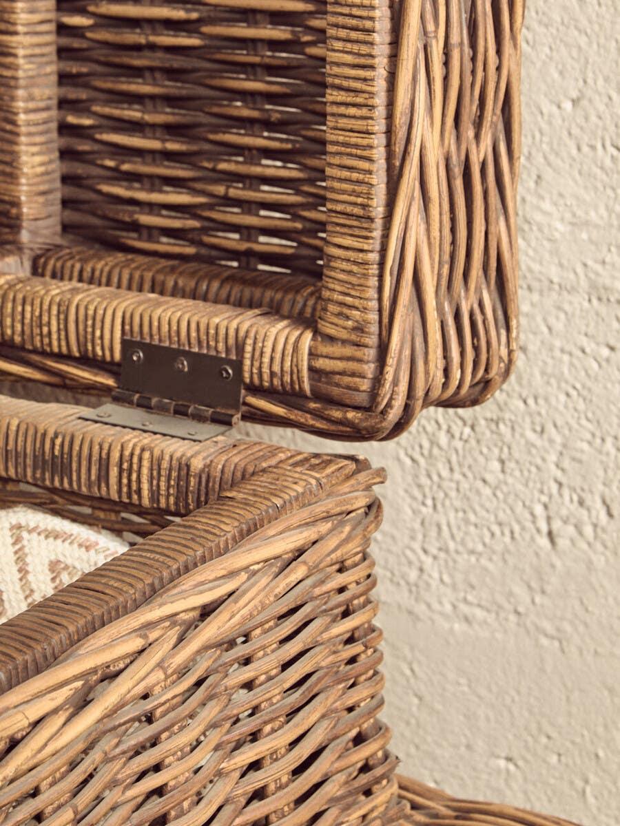 Closeup of open wicker storage basket with hinged lid against textured wall