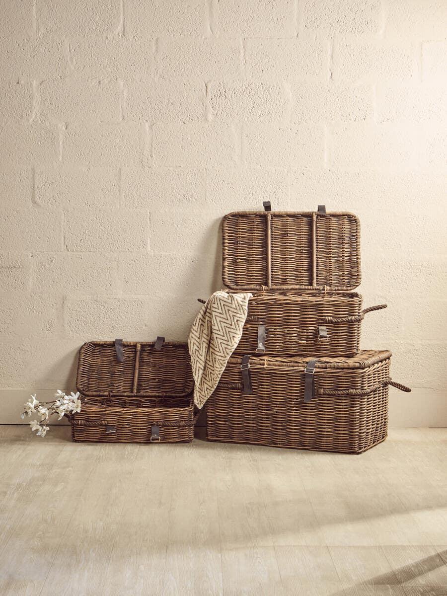 Set of three wicker storage baskets with lids and leather straps on wooden floor