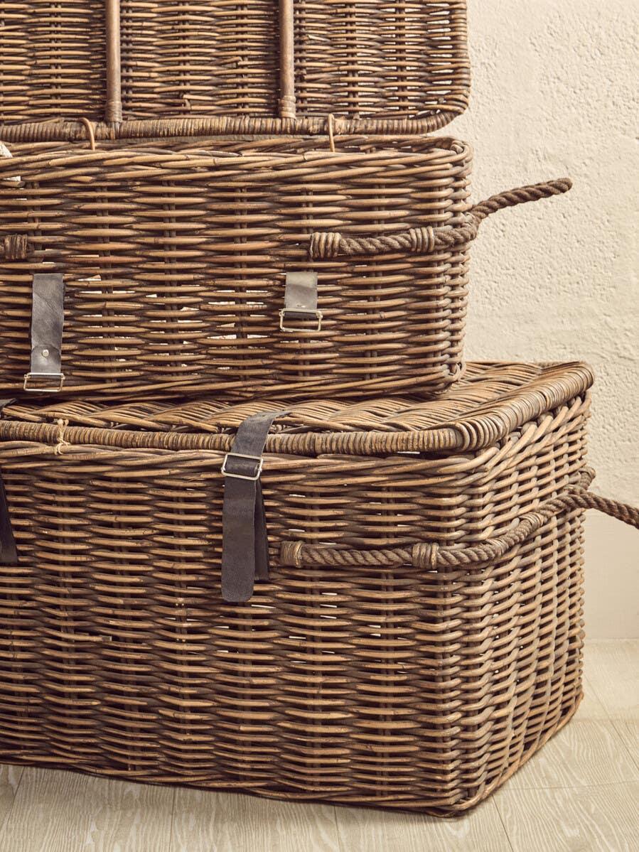 Stacked wicker storage baskets with rope handles and leather buckles on wood floor