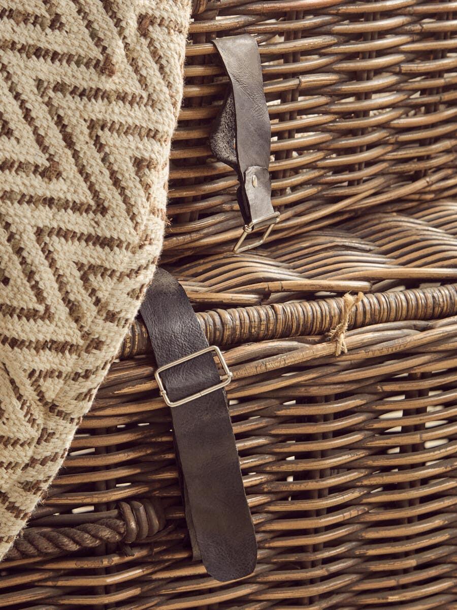 Wicker storage trunk with leather straps and textured beige throw draped over side