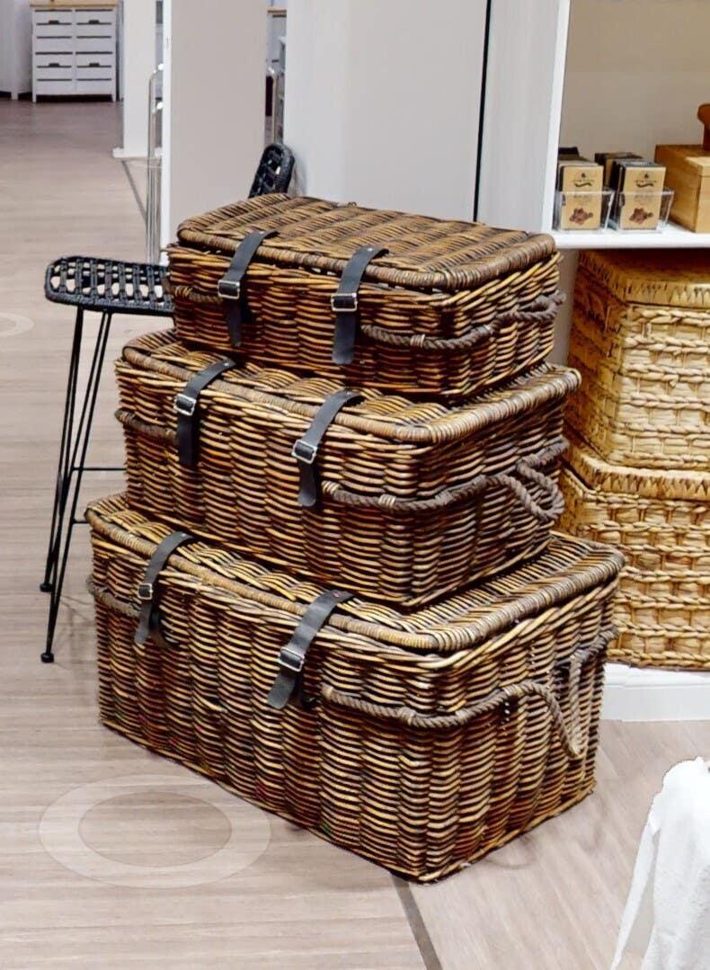 Stacked wicker storage baskets with lids and leather straps in showroom setting