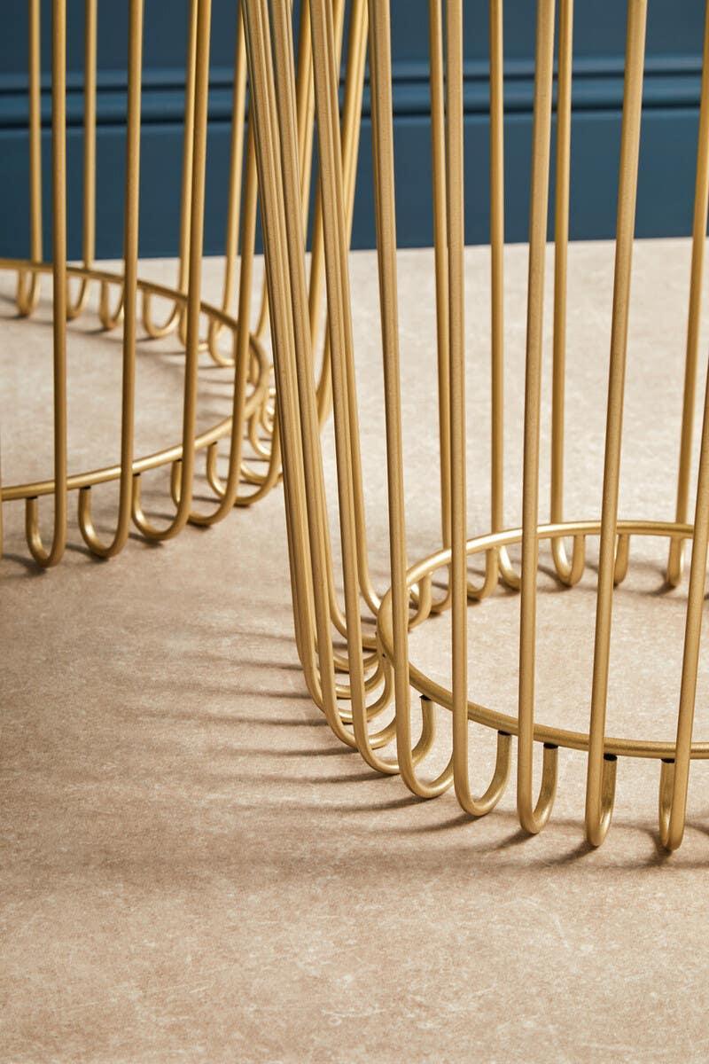 Gold metal side table base with vertical bars on beige floor