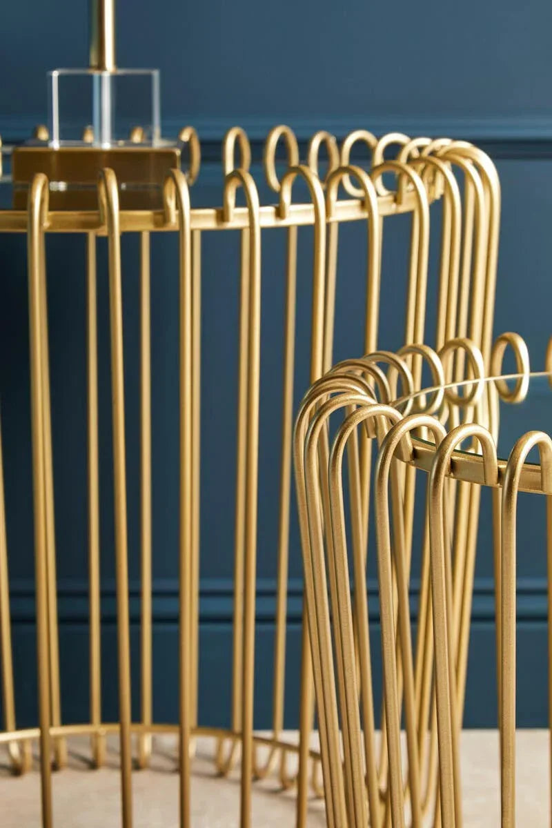 Gold metal side tables with curved wire frames against dark blue wall