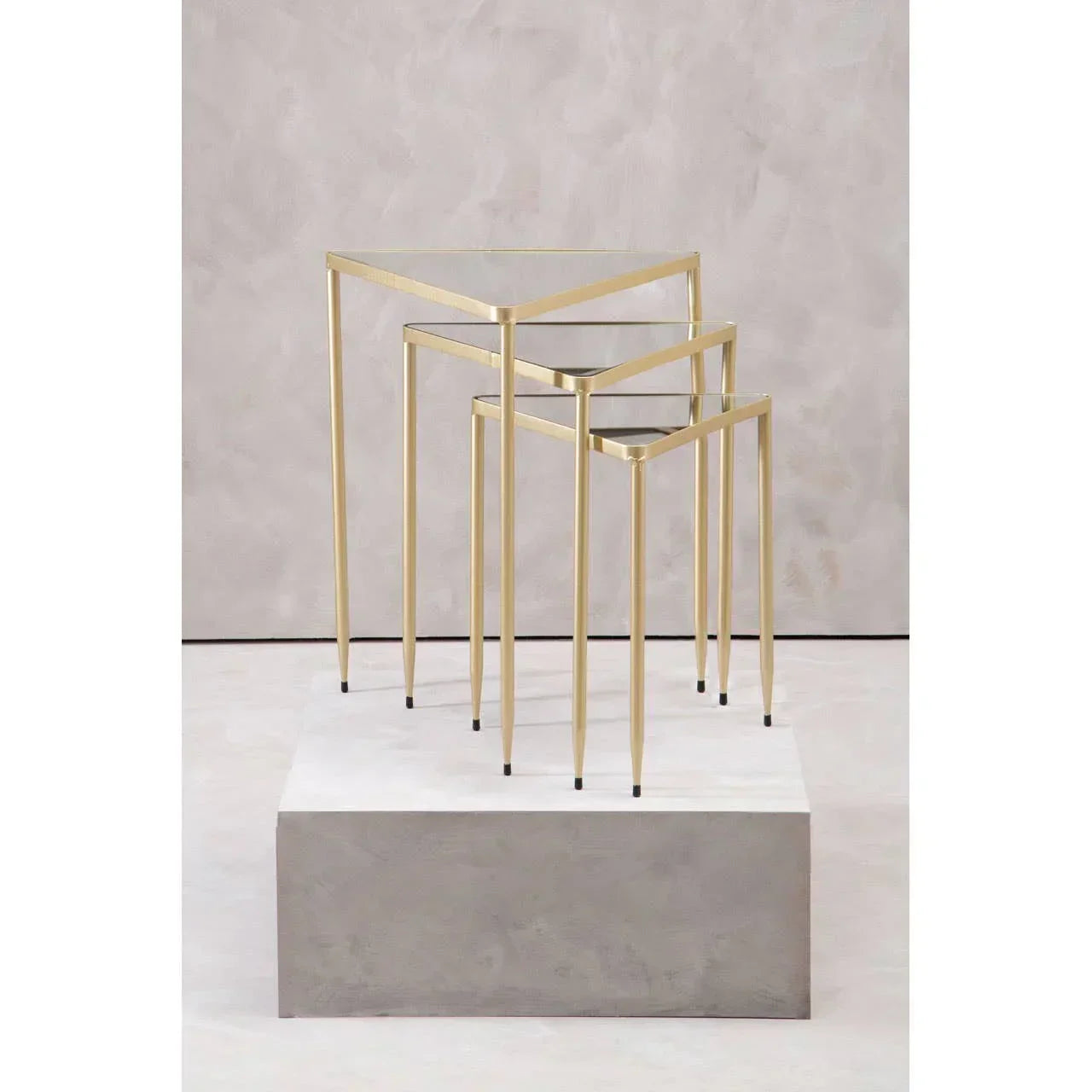 Set of three gold metal and glass nesting tables with slim legs on neutral background