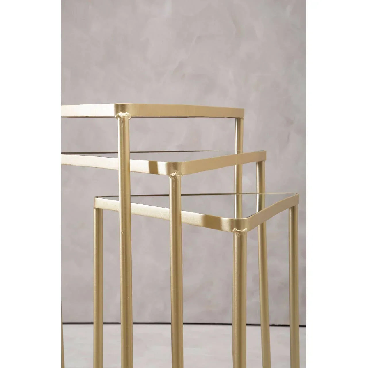 Set of gold metal nesting tables with glass tops against neutral background
