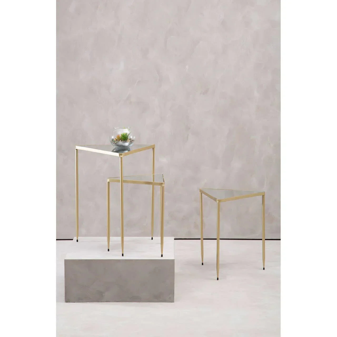 Set of three glass top nesting tables with gold metal frames on light background