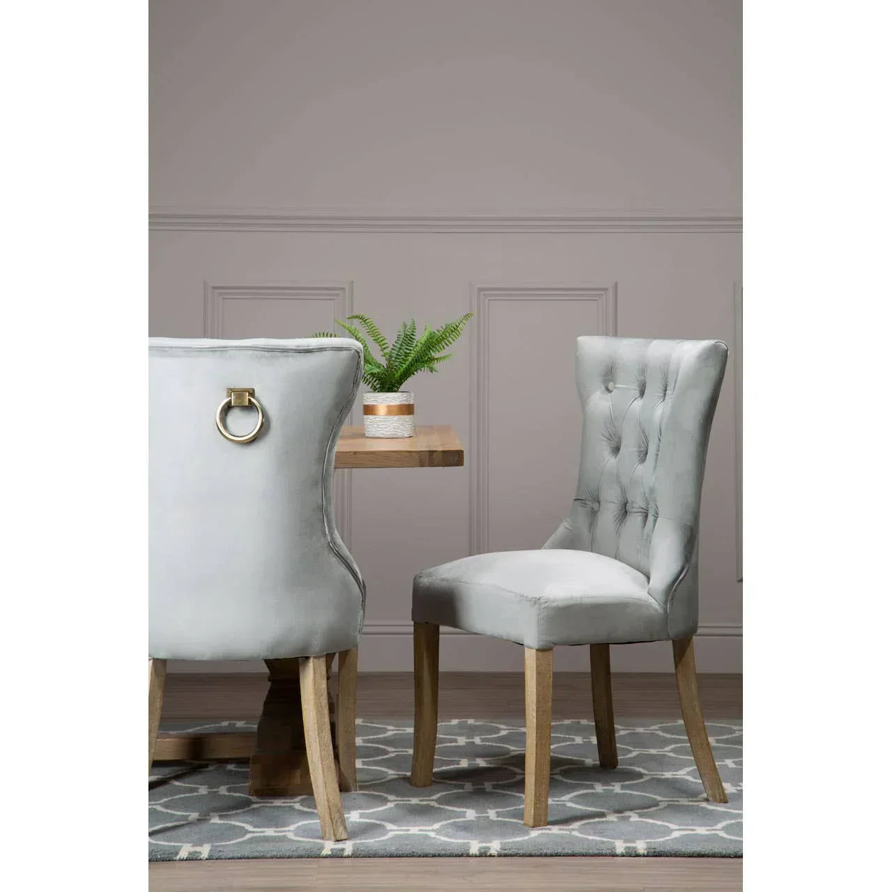 Grey velvet dining chair with button tufting and wooden legs beside wooden dining table