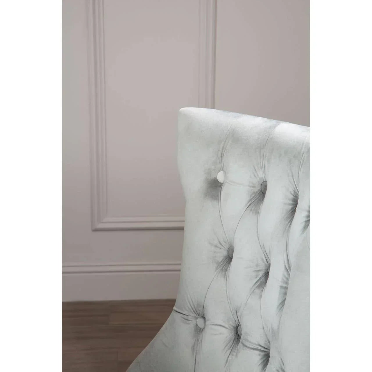 Light grey velvet dining chair with button-tufted backrest against a pale paneled wall