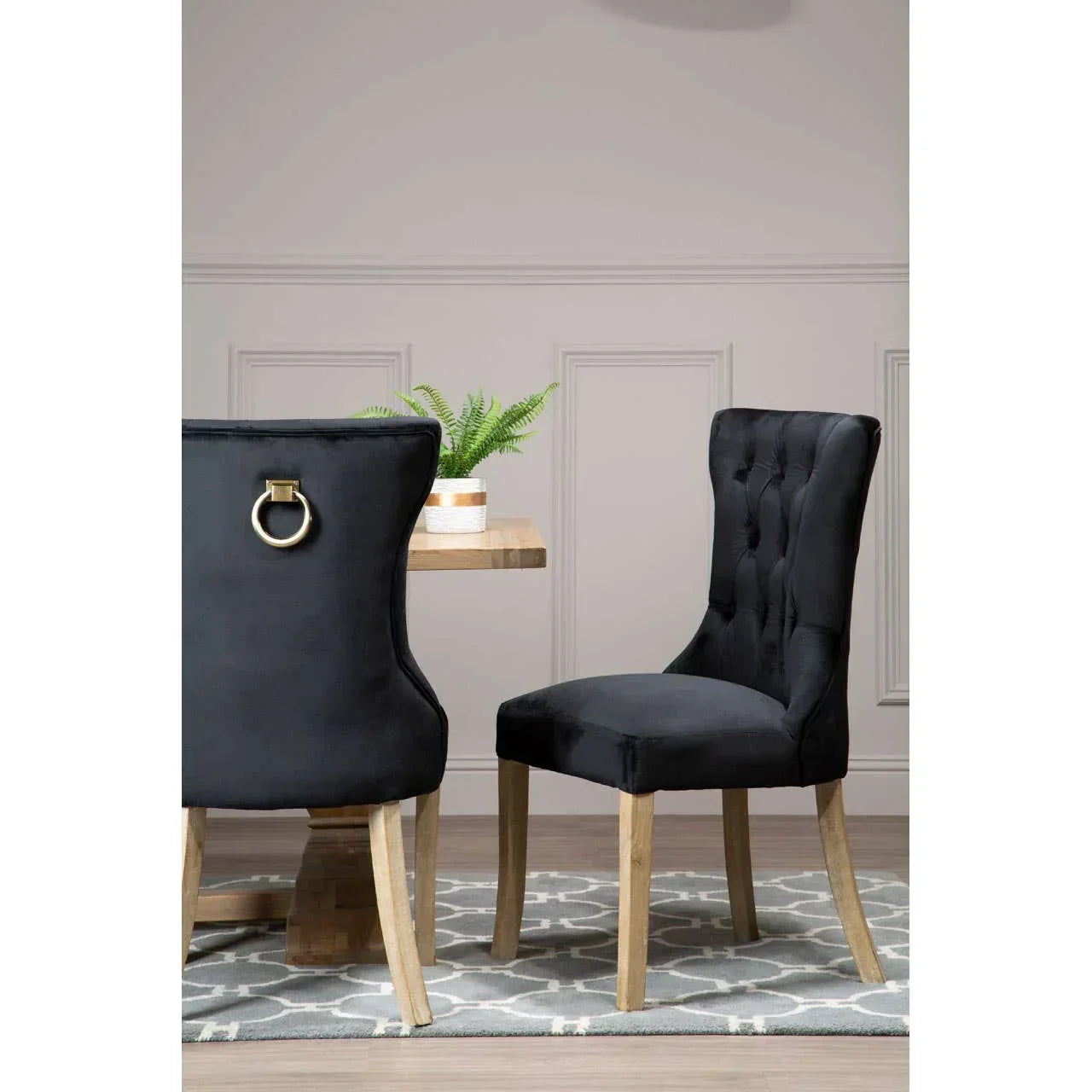 Black velvet dining chairs with tufted backs and light wood legs beside a wooden table