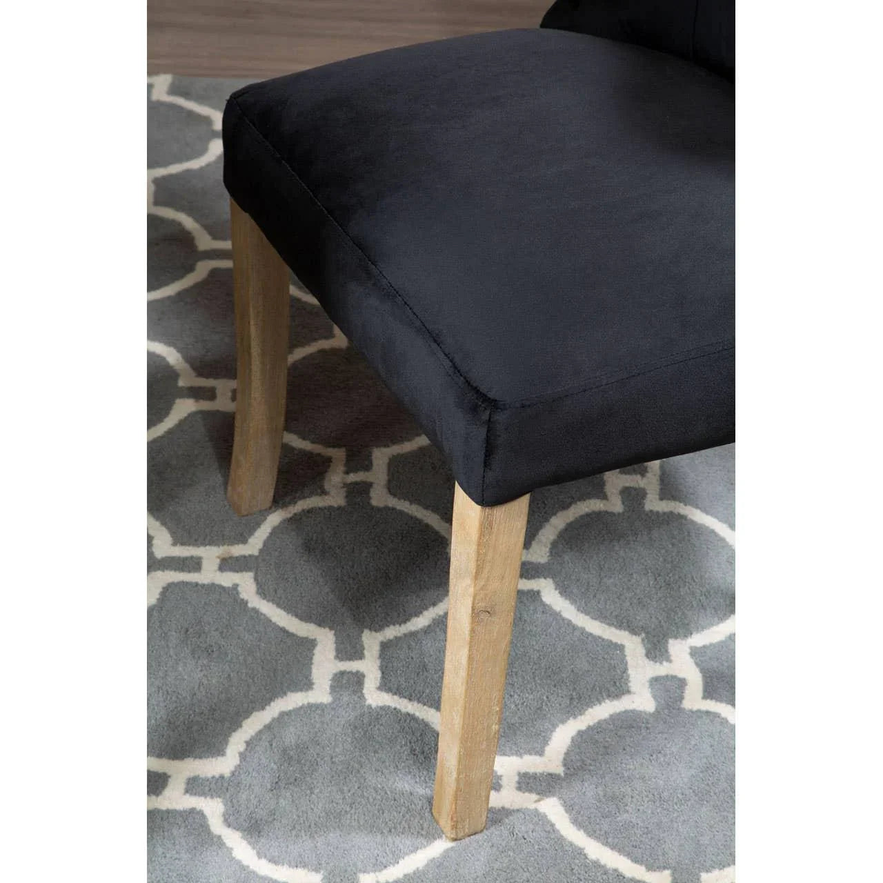 Black velvet chair seat with natural wood legs on patterned grey rug
