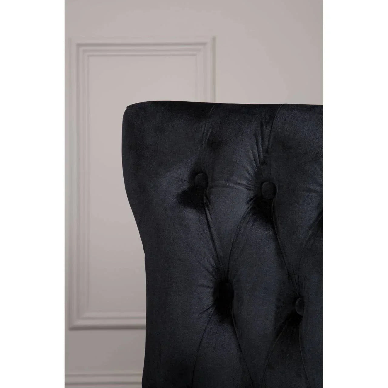 Black velvet dining chair with button-tufted backrest, close-up side view