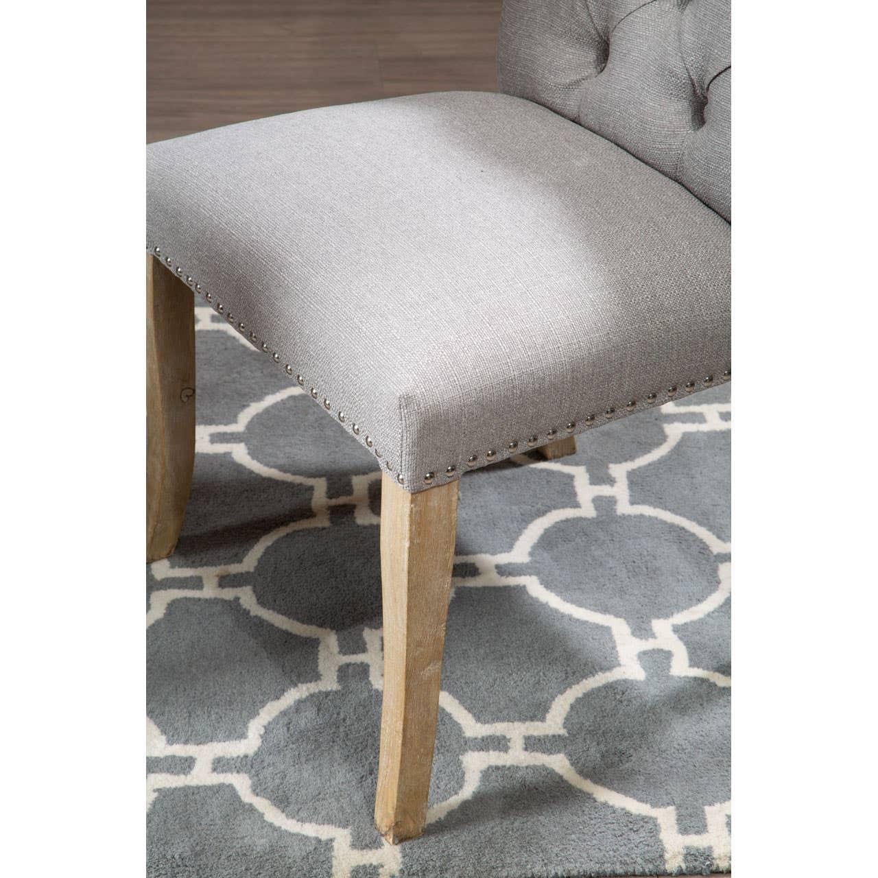 Grey upholstered dining chair with wooden legs, stud detailing, on patterned rug