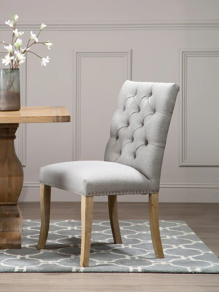 Grey upholstered dining chair with button back and wooden legs on patterned rug