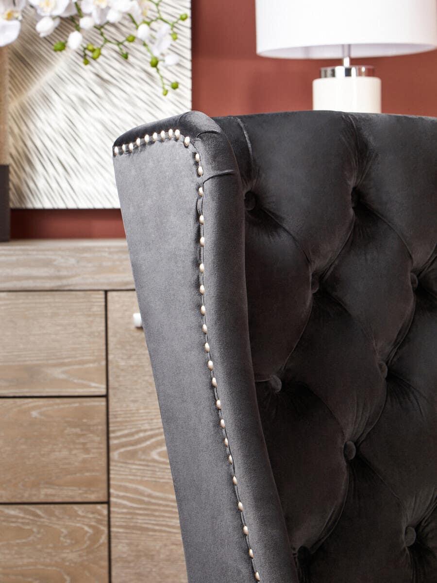 Charcoal velvet dining chair with button tufting and nailhead trim beside wooden sideboard