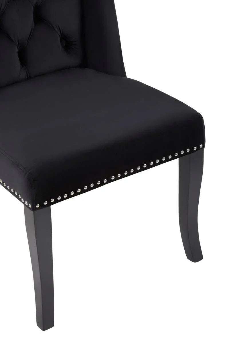 Black upholstered dining chair with studded trim and tufted backrest, angled view