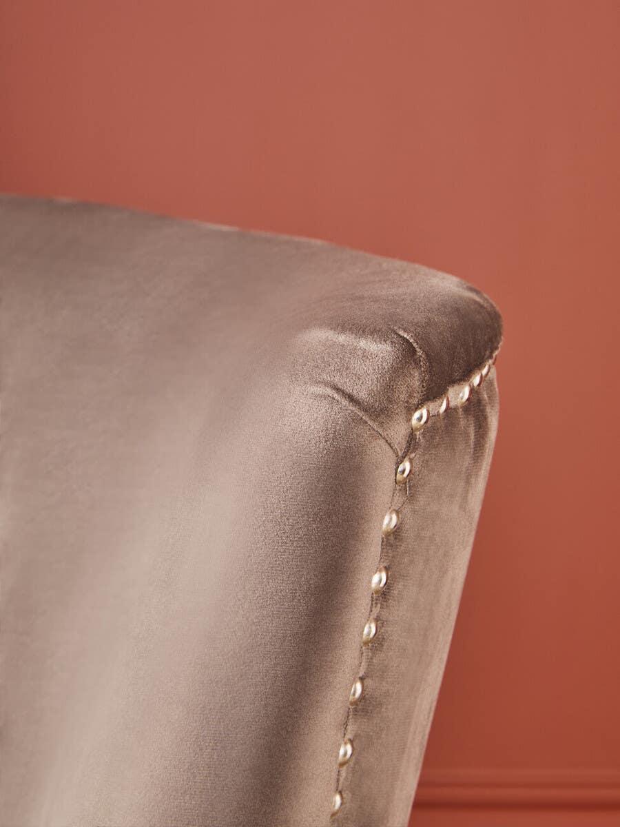 Velvet dining chair armrest with silver stud detailing against terracotta wall