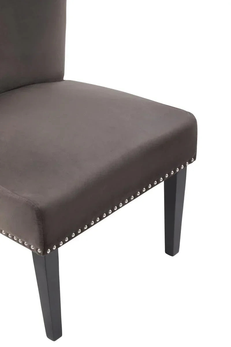Grey upholstered dining chair with nailhead trim and dark wood legs, close-up side view