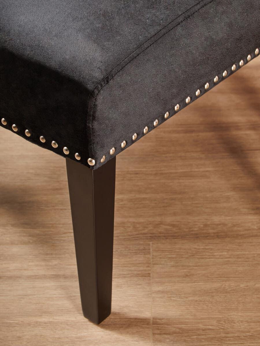 Black upholstered dining bench with metal stud detailing and dark wooden leg on wood floor