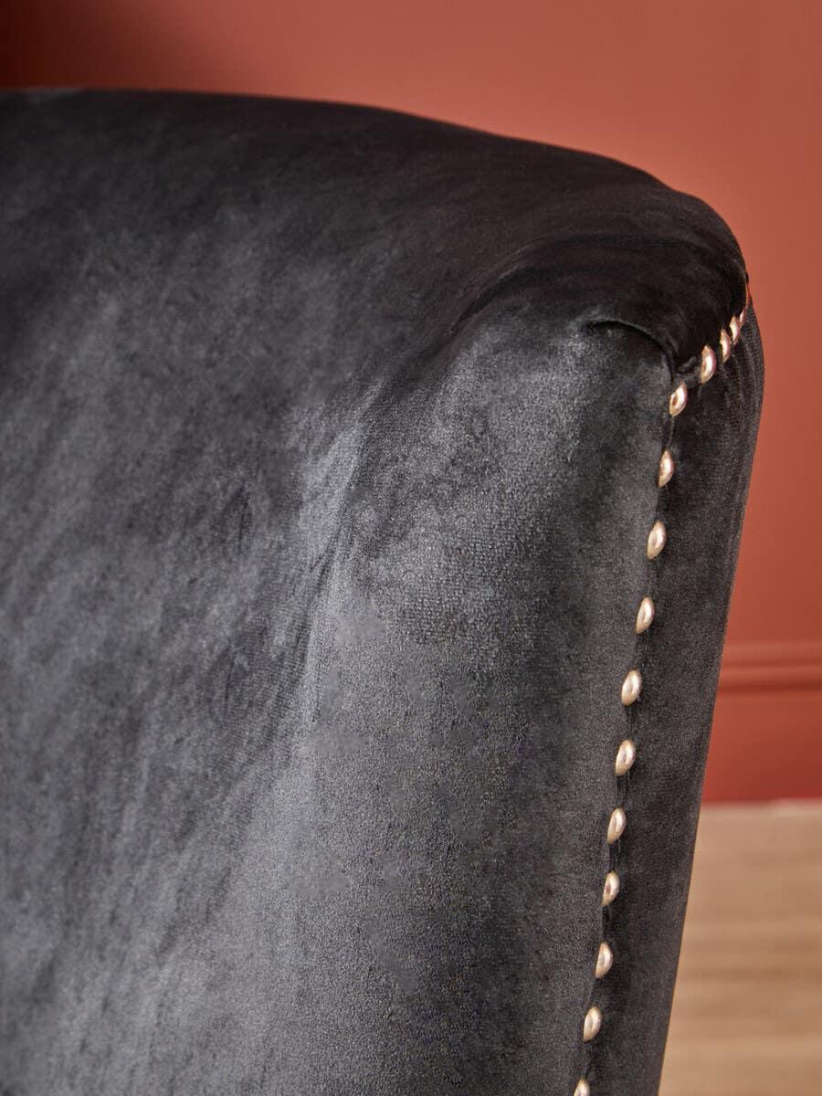 Close-up of black velvet sofa arm with brass stud detailing against terracotta wall