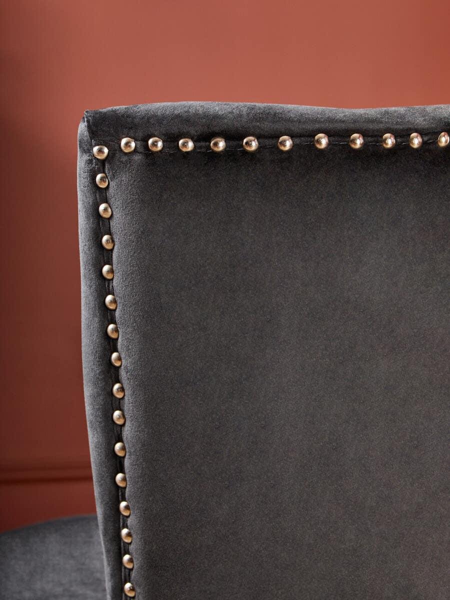 Close-up of dark grey velvet dining chair with silver studded trim against terracotta wall
