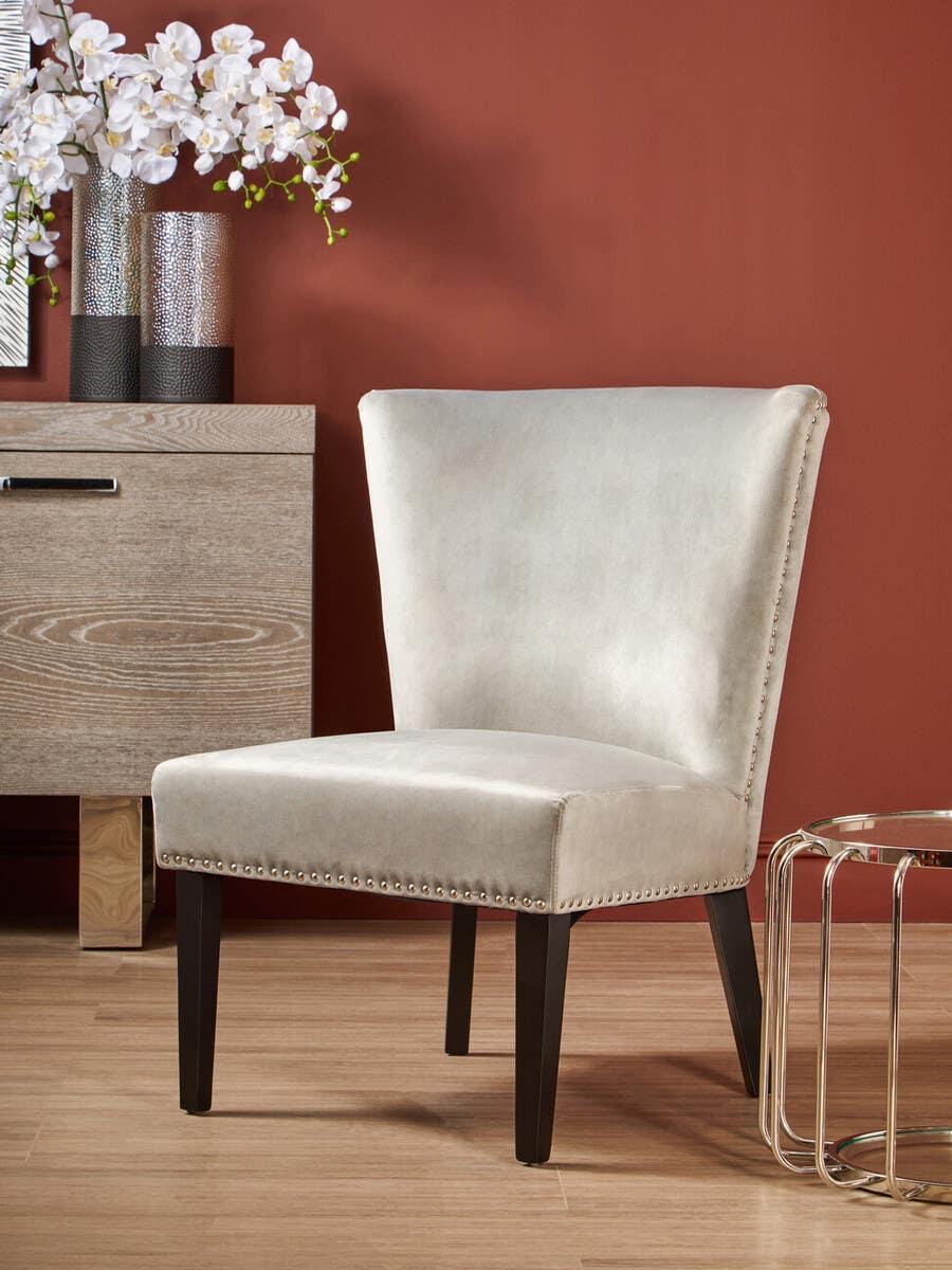 Upholstered accent chair with studded trim and dark wooden legs beside modern side table