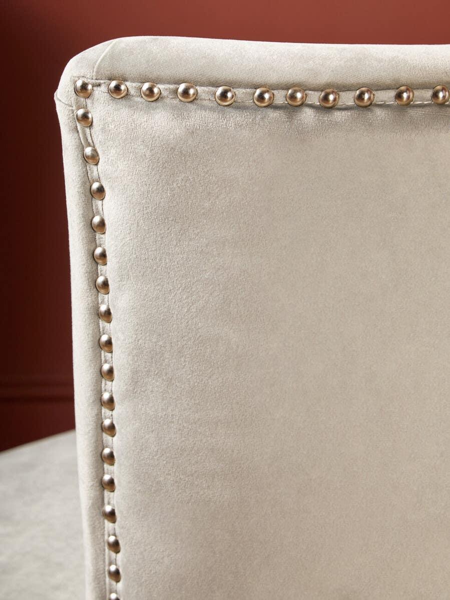Beige velvet dining chair back with metallic stud detailing against a red wall
