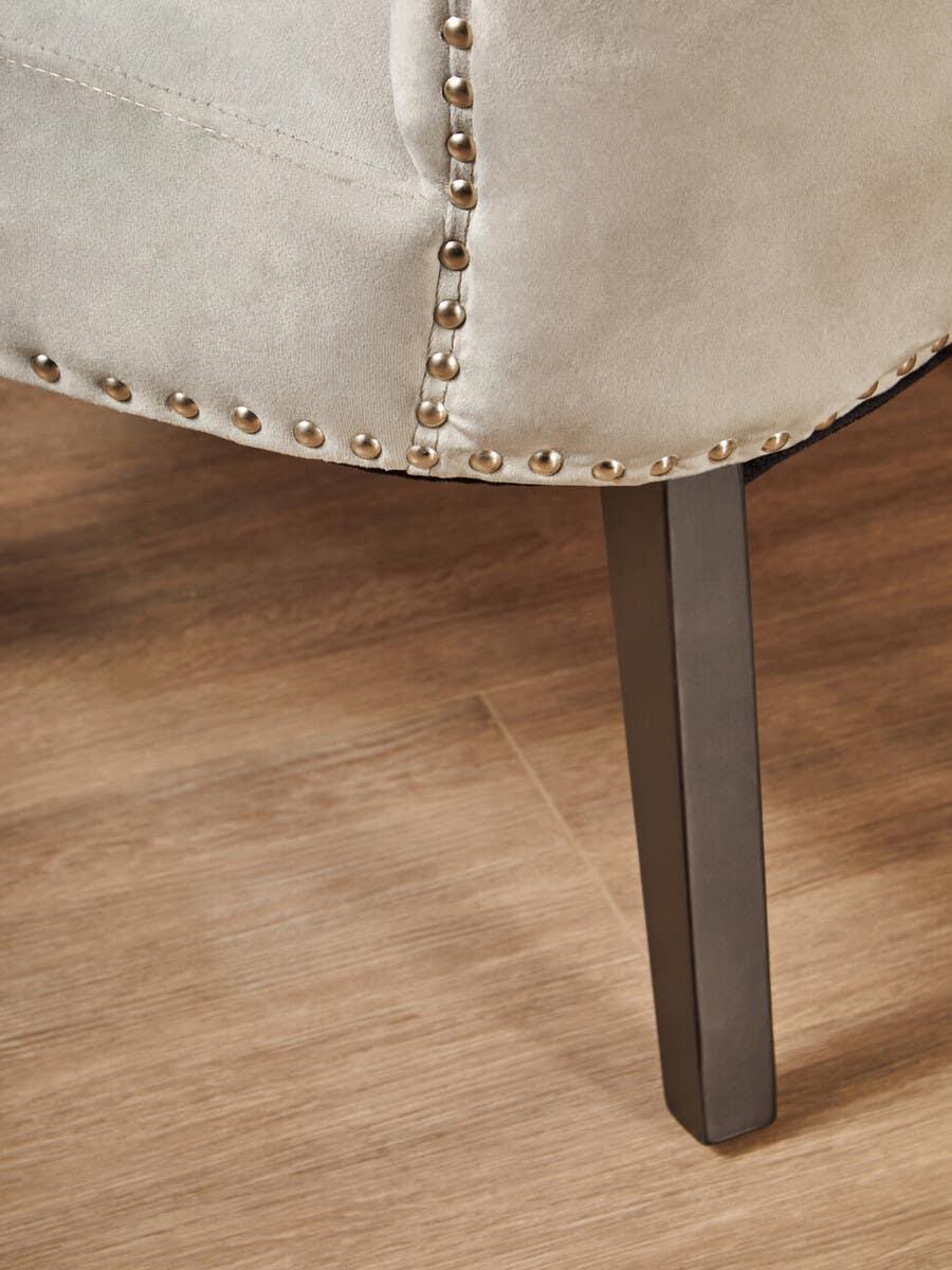 Closeup of beige fabric sofa with metal stud detail and dark wooden leg on wood floor