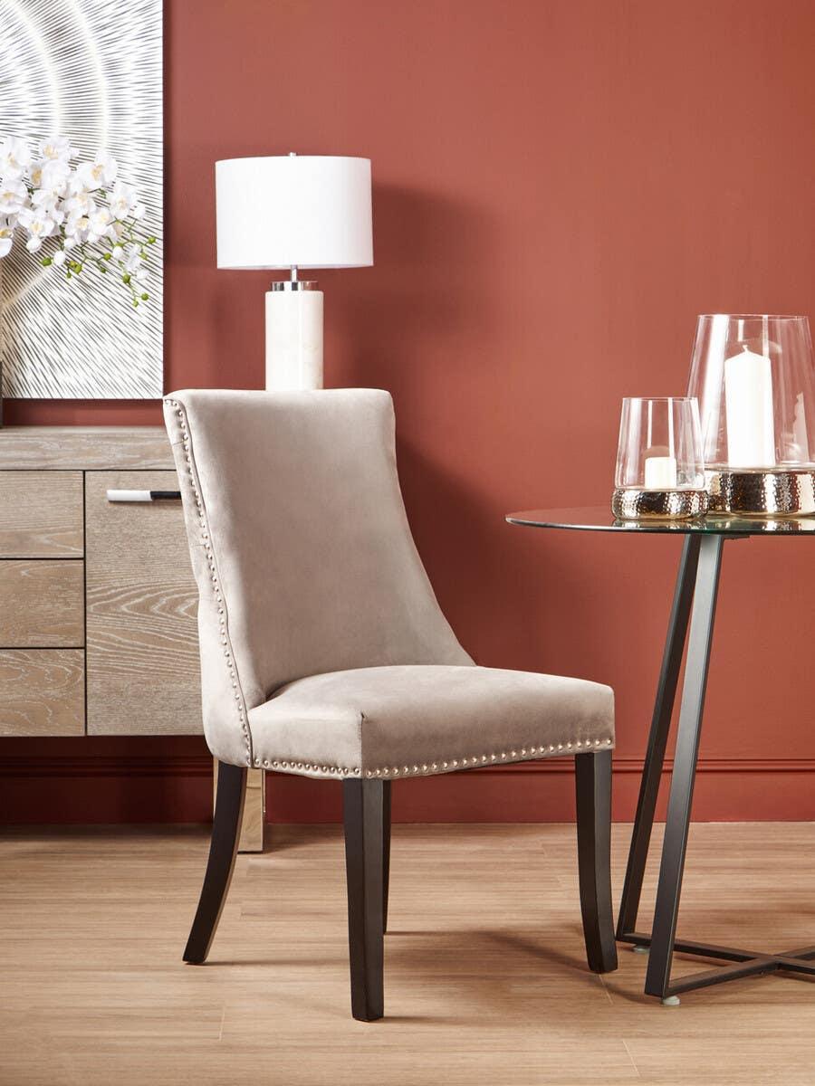 Taupe velvet dining chair with silver stud trim beside round glass table on wood floor