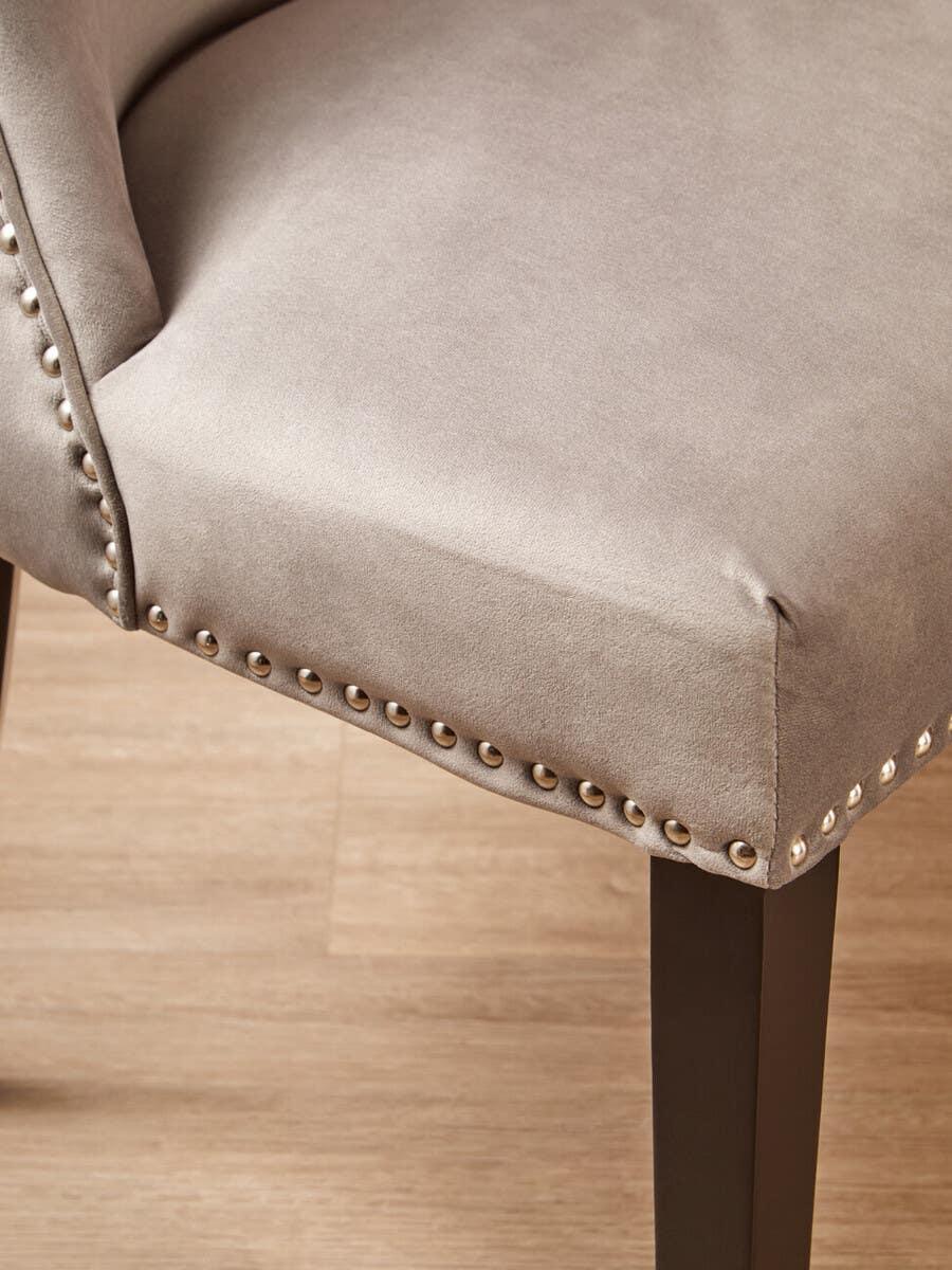 Grey upholstered dining chair with metal stud detailing and dark wood legs on wooden floor