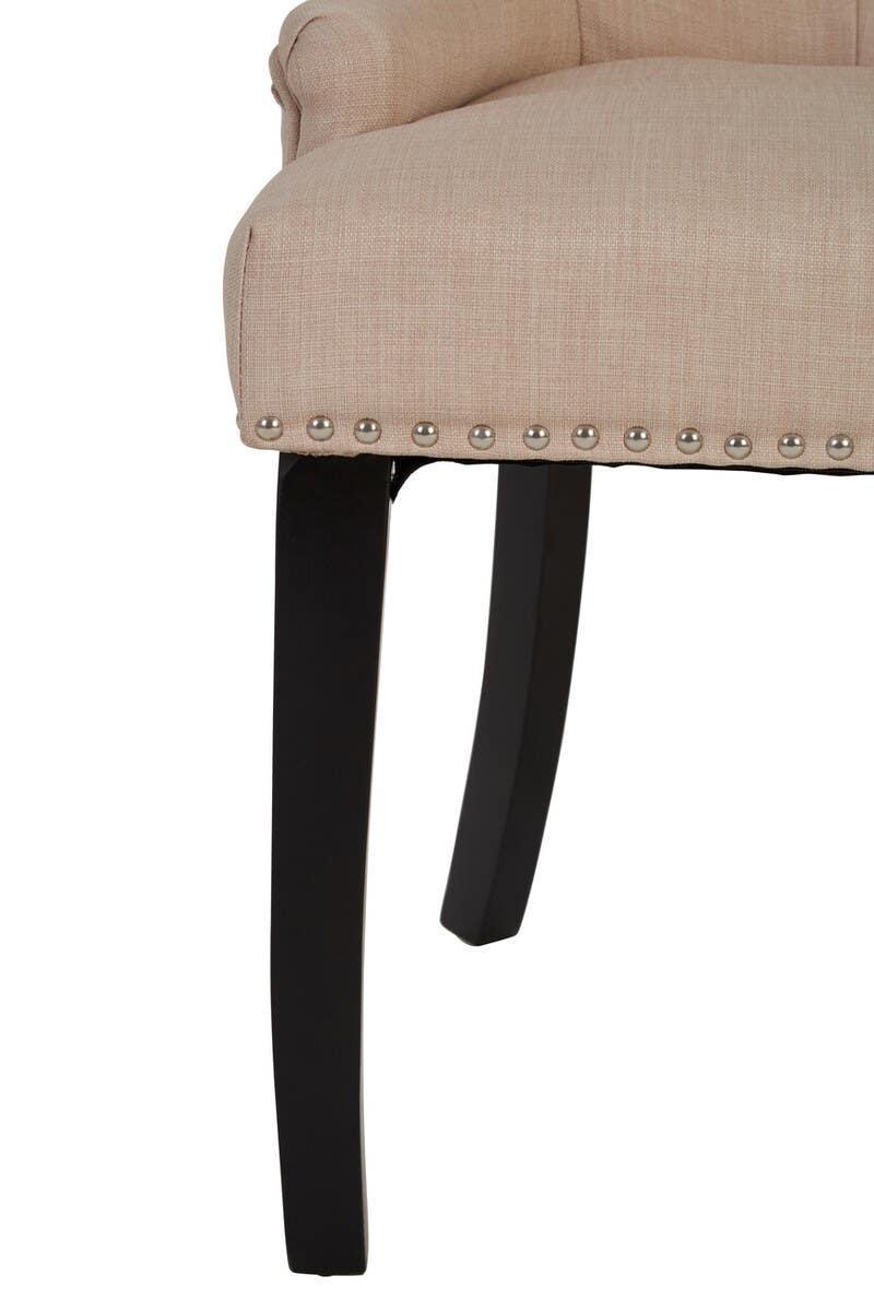 Beige upholstered dining chair seat with silver stud trim and black wooden legs, close view