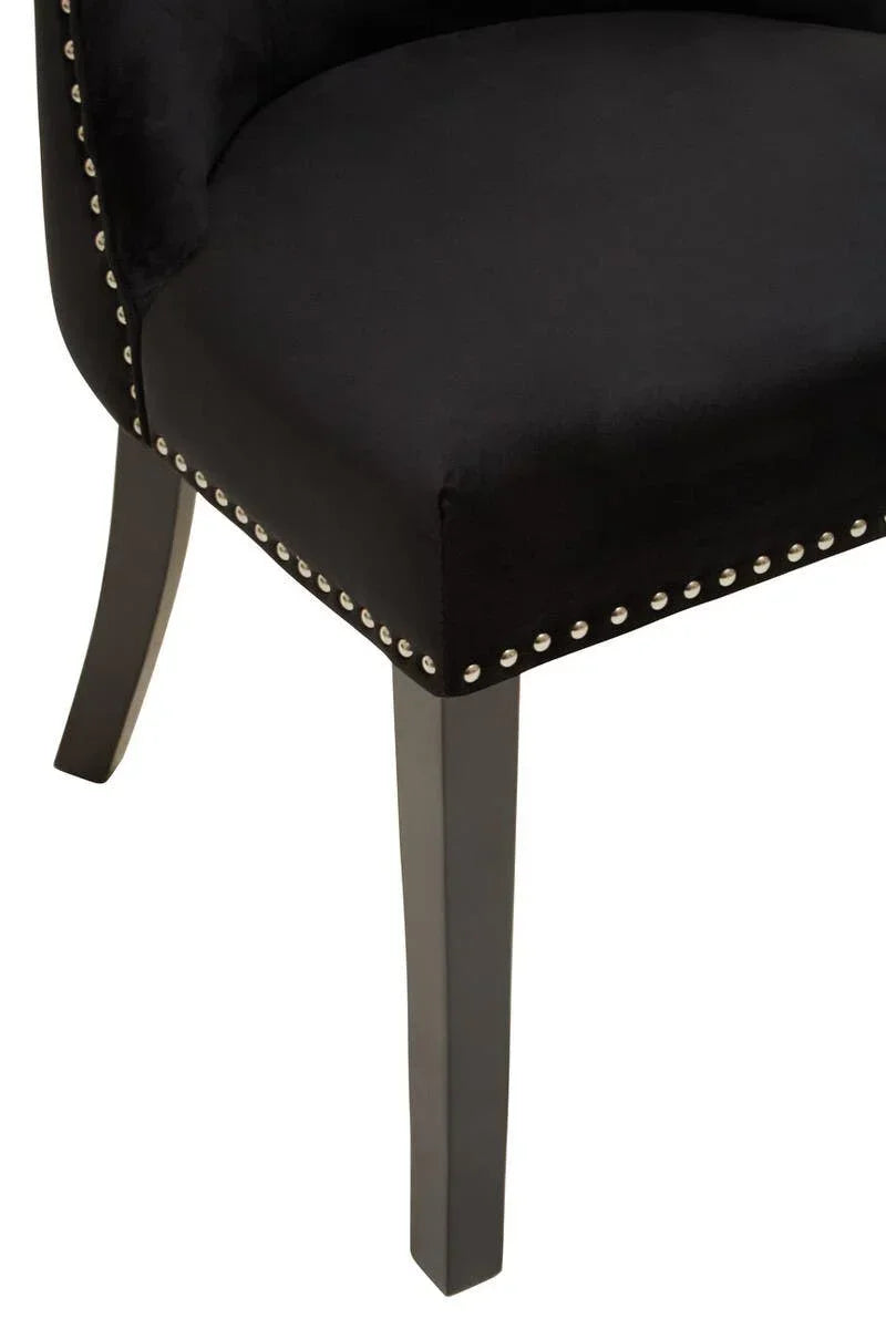 Black velvet dining chair corner with silver stud trim and wooden legs closeup