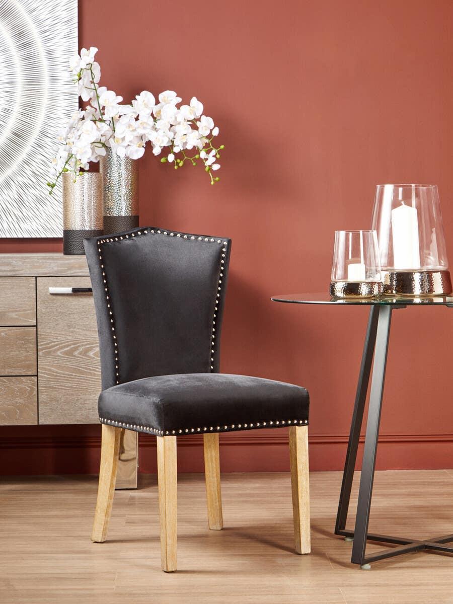 Black velvet dining chair with studded trim and light wood legs in modern dining room