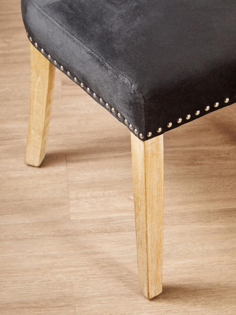 Grey velvet dining chair seat with wooden legs and nailhead trim on wood floor