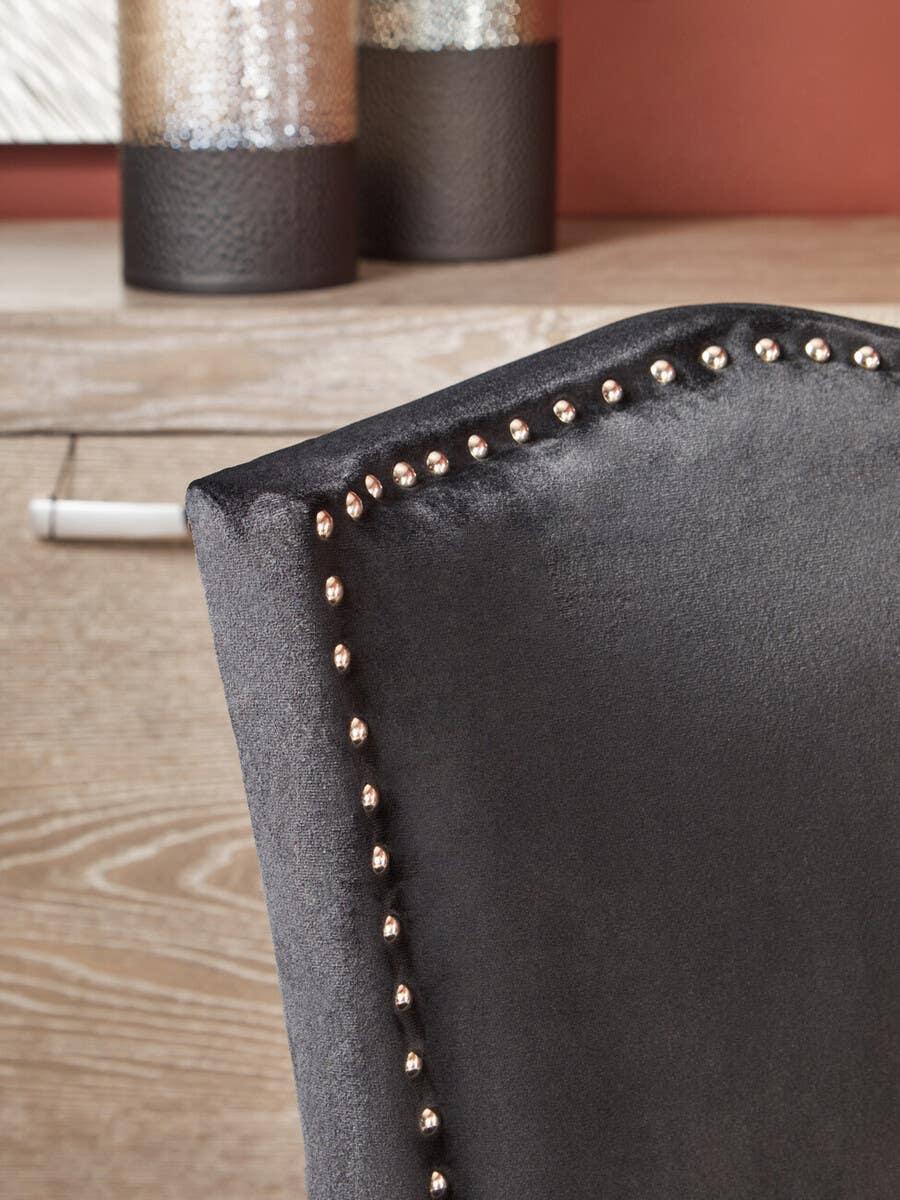 Dark grey velvet dining chair with silver stud trim near wooden table