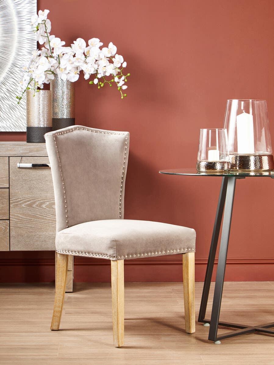 Velvet dining chair with stud detail and wooden legs against a terracotta wall