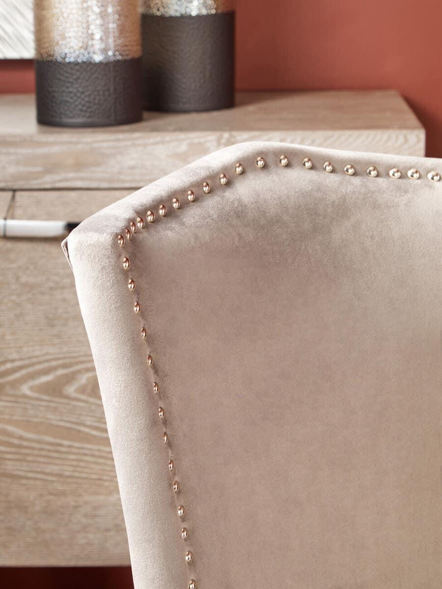 Beige velvet dining chair with nailhead trim detail beside light wood table