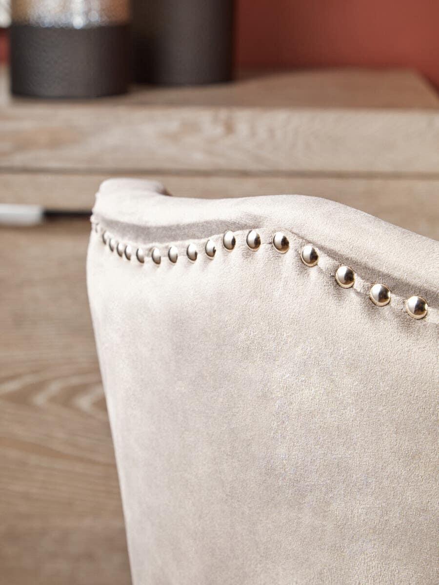 Beige upholstered dining chair with silver stud detailing on curved backrest