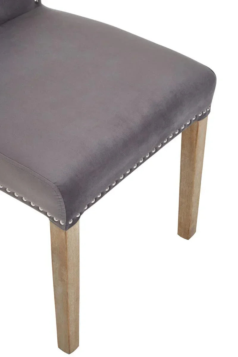 Grey velvet dining chair with silver stud trim and wooden legs, side angle view