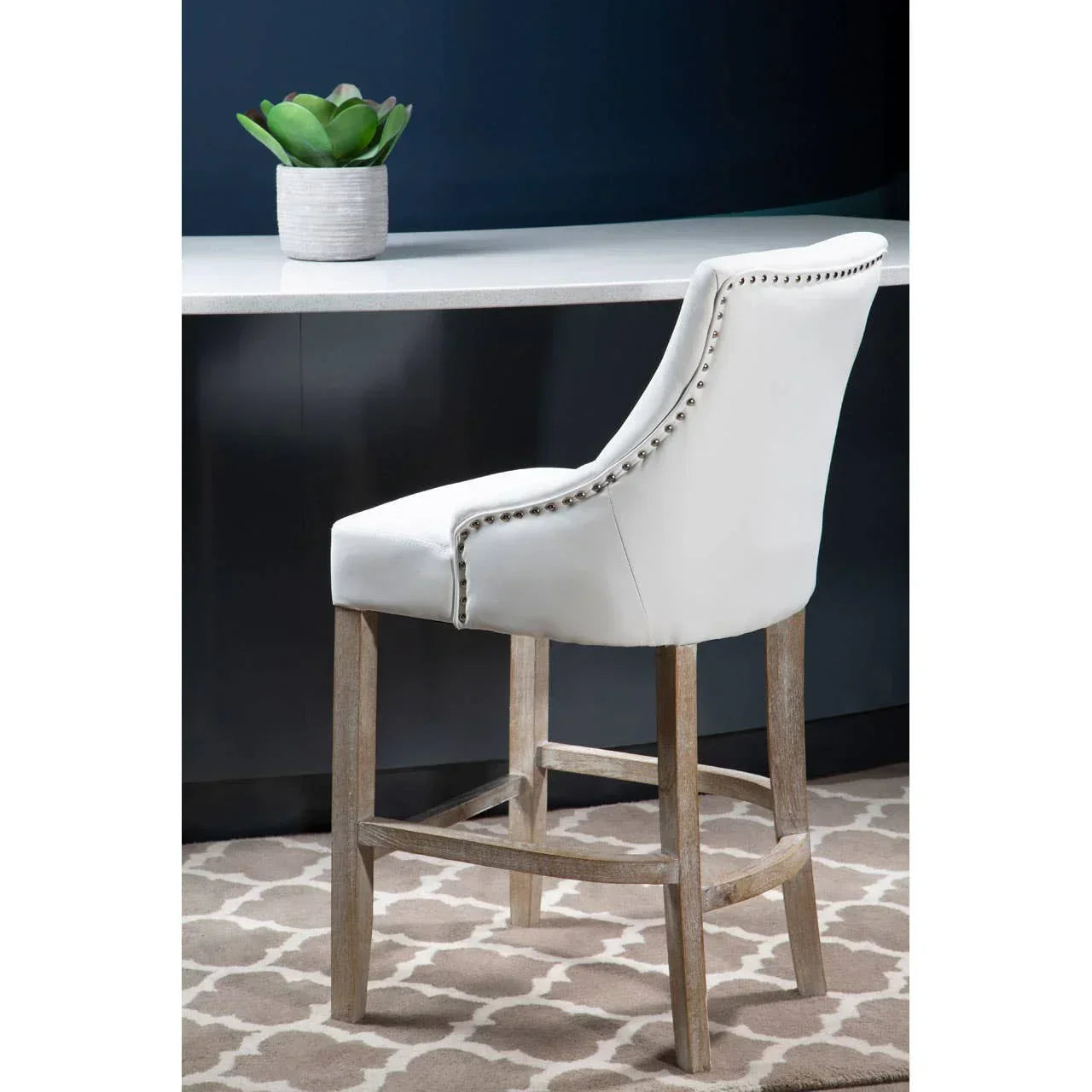 White upholstered bar stool with silver stud detail and wooden legs at kitchen counter