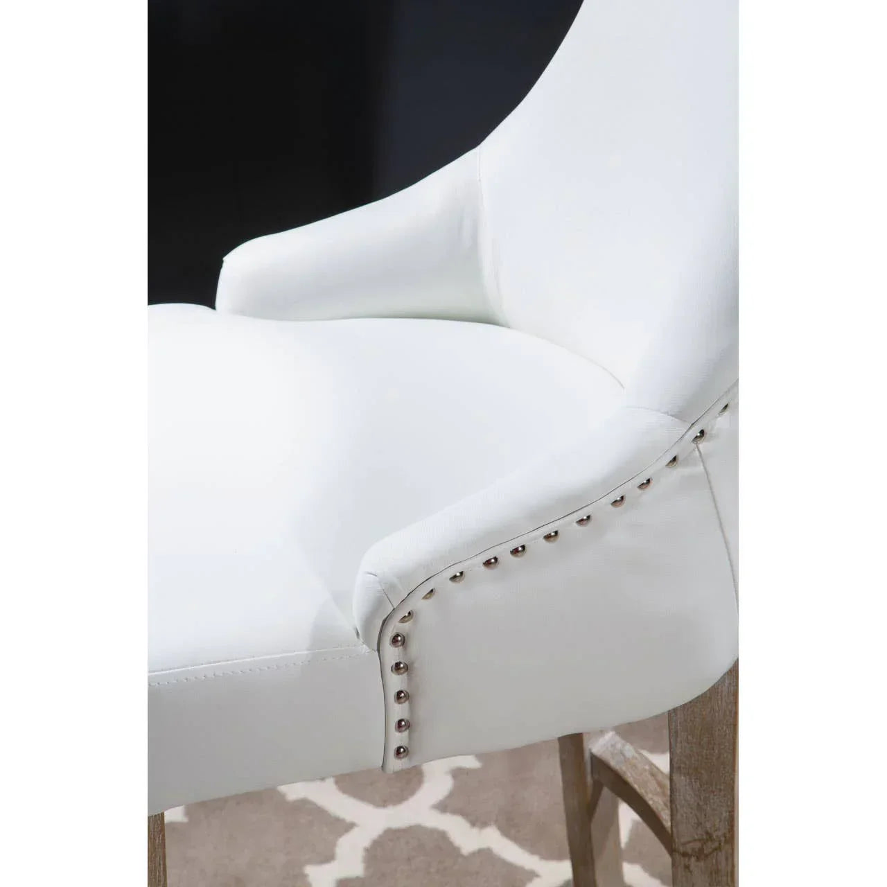 White upholstered dining chair with nailhead trim and wooden legs on patterned rug