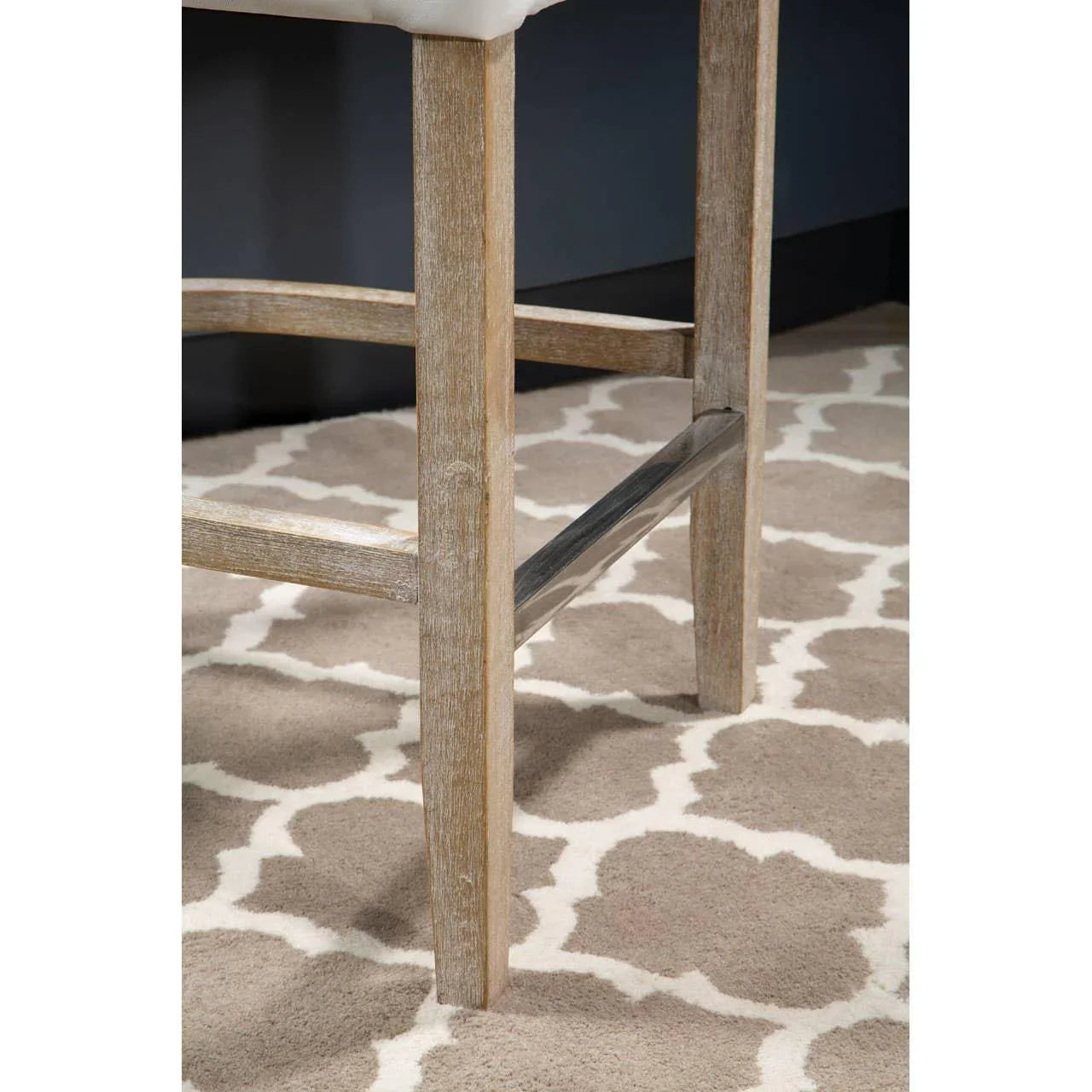 Light wood bar stool legs with metal footrest on patterned rug