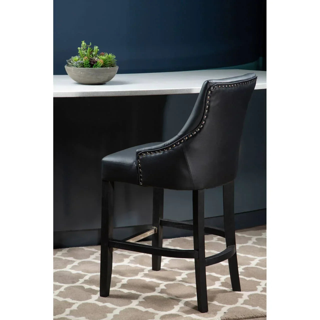 Black leather bar stool with nailhead trim and dark wood legs beside a kitchen counter