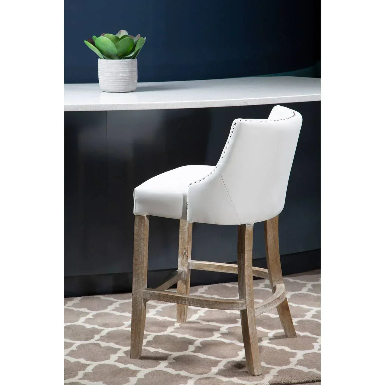 White bar stool with wood legs and nailhead trim at kitchen counter