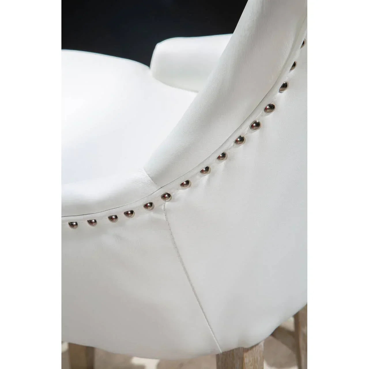 White upholstered dining chair with silver stud detailing and wooden legs, close view