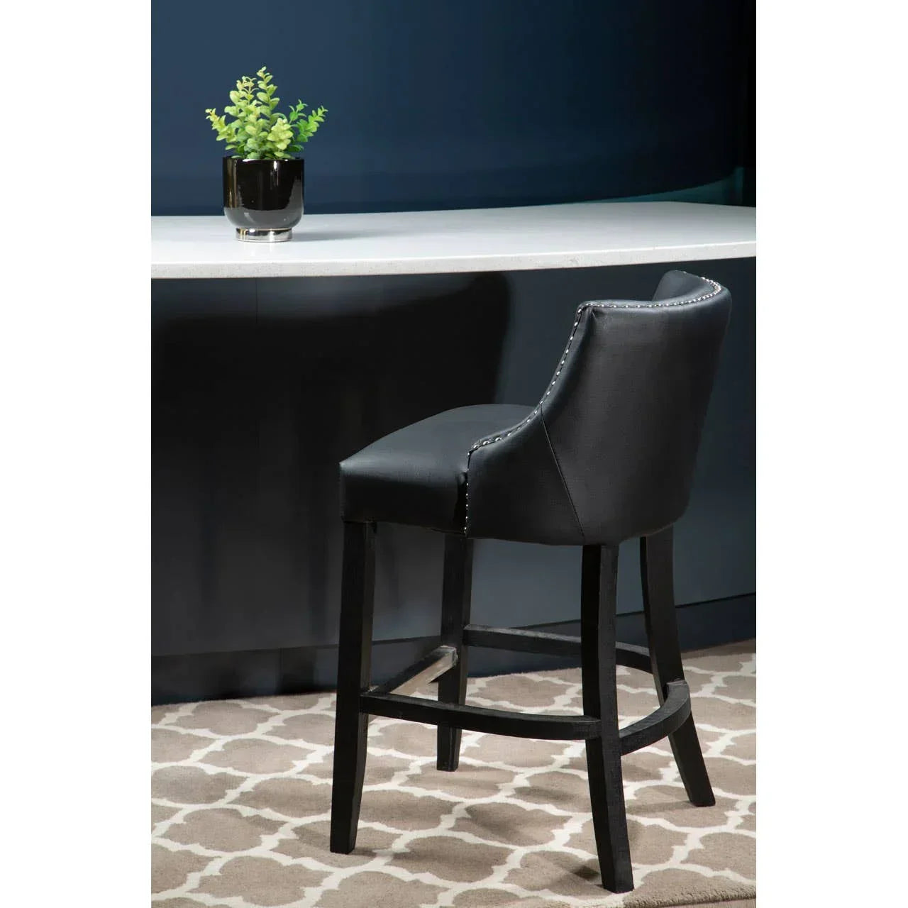 Black leather bar stool with studded trim at kitchen counter on patterned rug