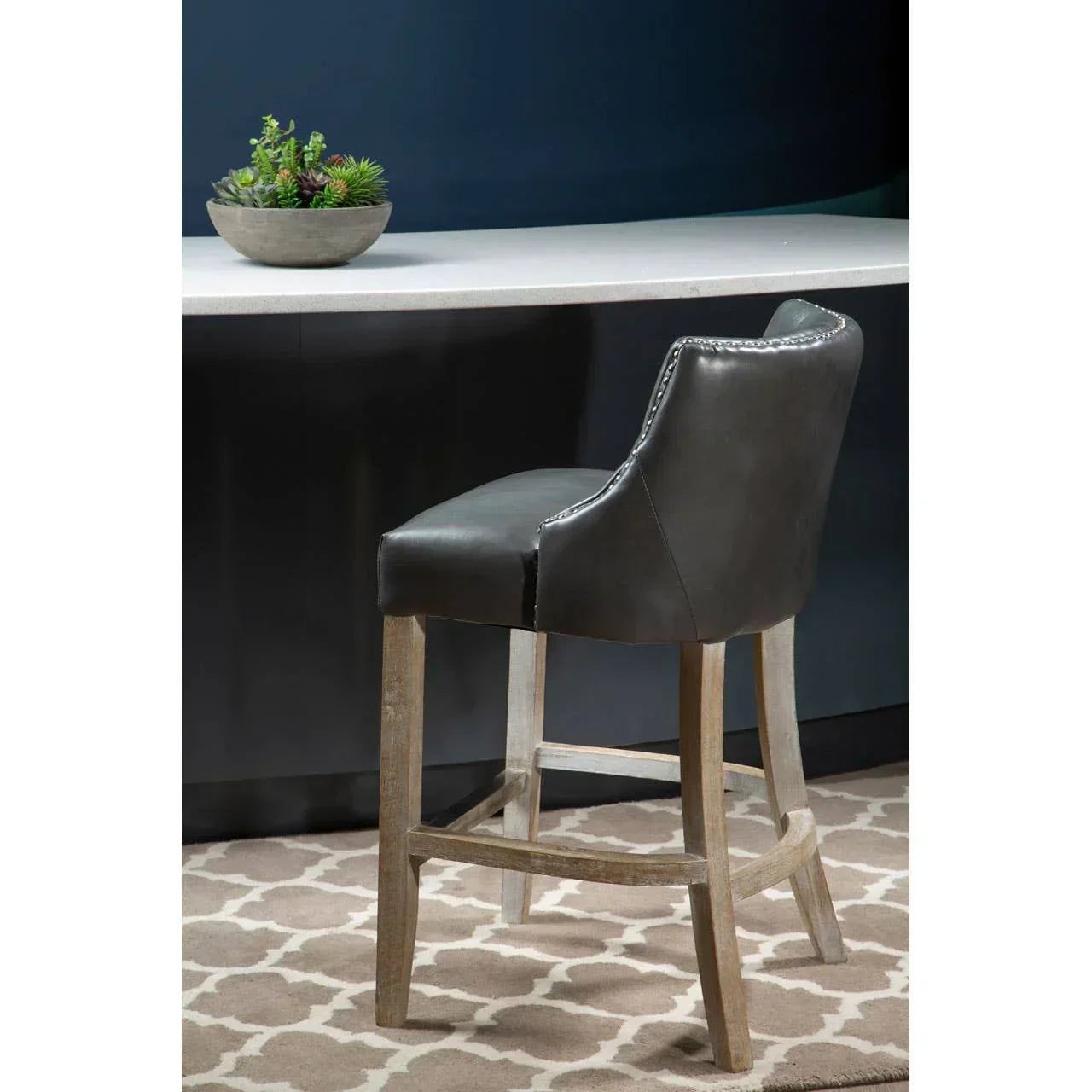 Black leather bar stool with wooden legs beside counter, nailhead trim on backrest